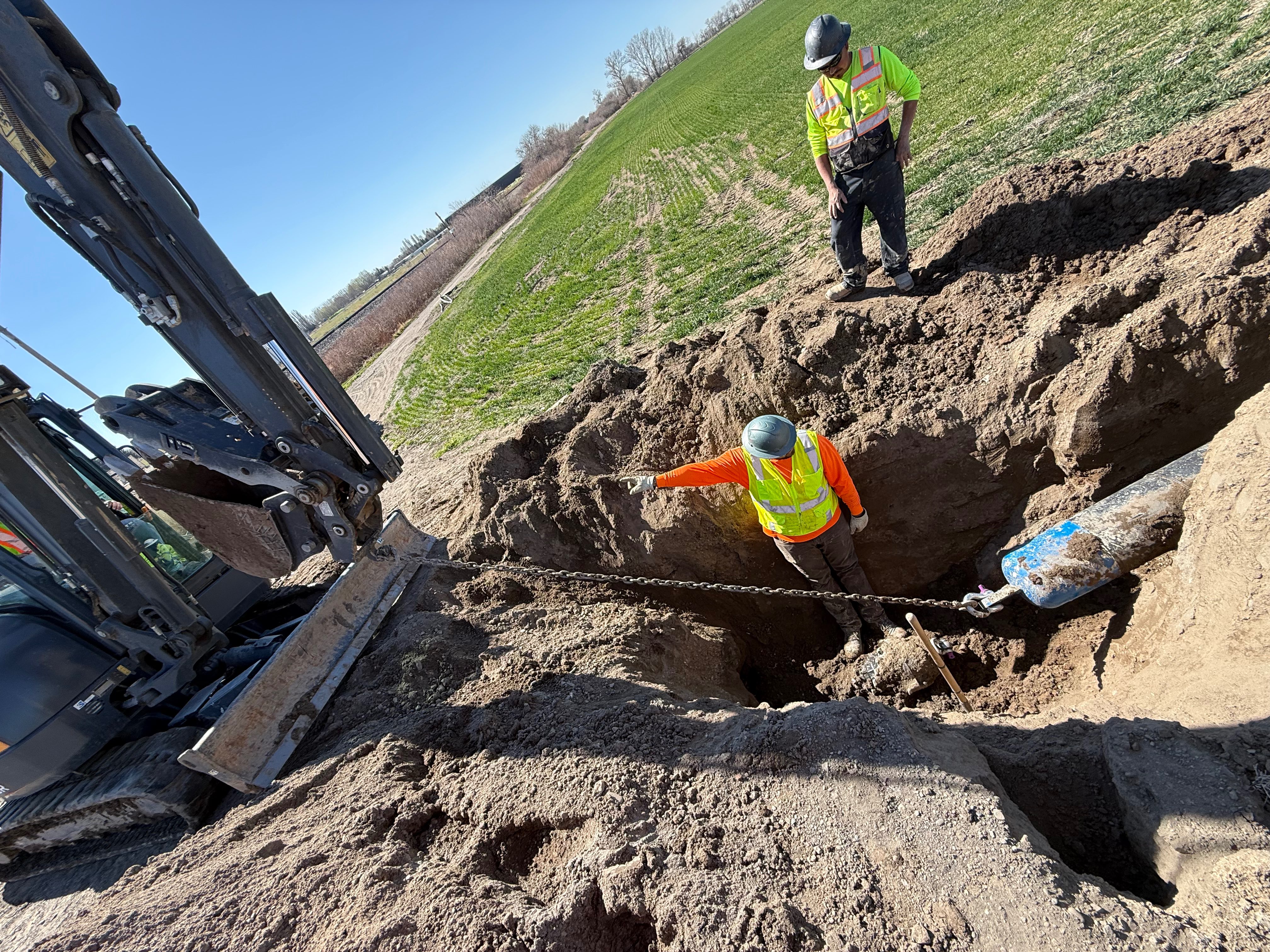 Power distribution crew excavating utility trench in agricultural field